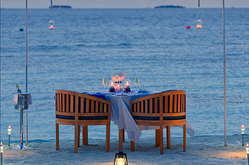 Cena privada en la playa con mesa iluminada por velas en Bandos Maldives